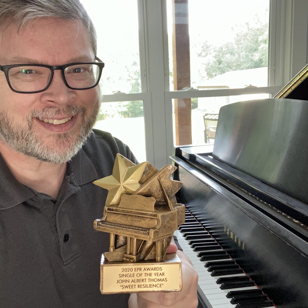 John Albert Thomas at the piano, holding the EPR Single of the Year award for 'Sweet Resilience'